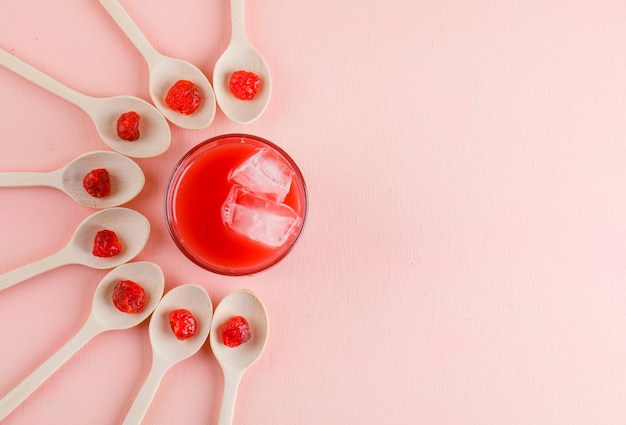 Juice with dried cherry in a glass on pink surface, top view.