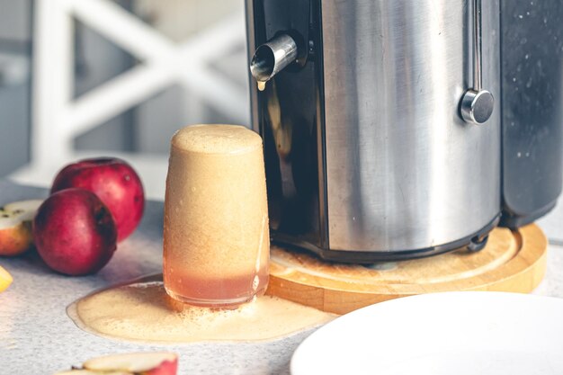 Соковыжималка и стакан с яблочным соком на кухонном столе