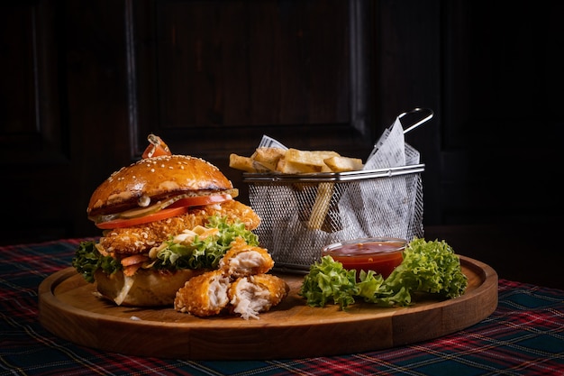 Juicy chicken burger with fresh lettuce and crispy french fries on a wooden board