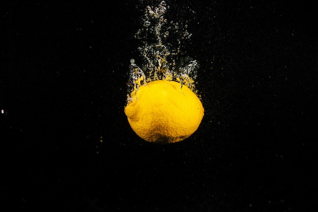 Сочный лимон падает в воду на черном фоне