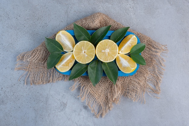 Сочные дольки лимона и листья на синем блюде на мраморном фоне.
