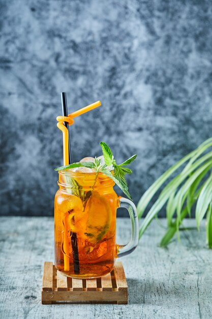 Juicy lemonade with straw and mint on the plant surface 