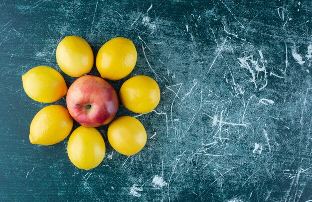Сочные лимоны и красное яблоко на мраморном столе.