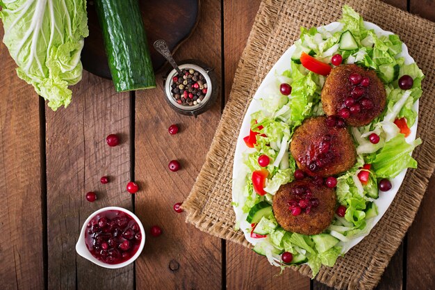 Juicy meat cutlets with cranberry sauce and salad on a wooden table in a rustic style. Top view