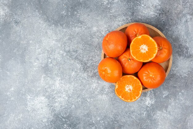 Сочные апельсиновые фрукты с дольками в деревянной тарелке на каменном столе.