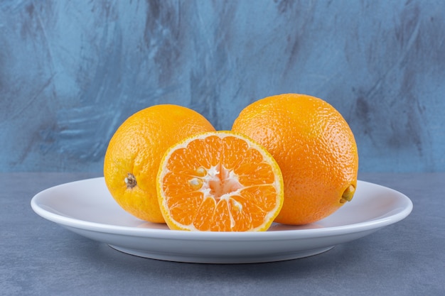 Сочные апельсины на тарелке, на темной поверхности