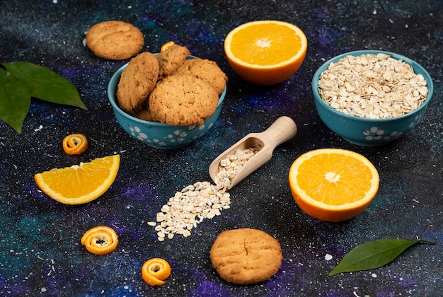 Free photo juicy oranges with cookie and oatmeal over dark table.