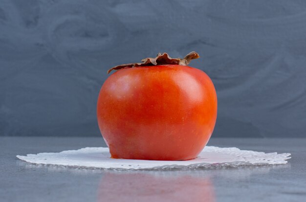 Juicy persimmon on a doily on marble background. 