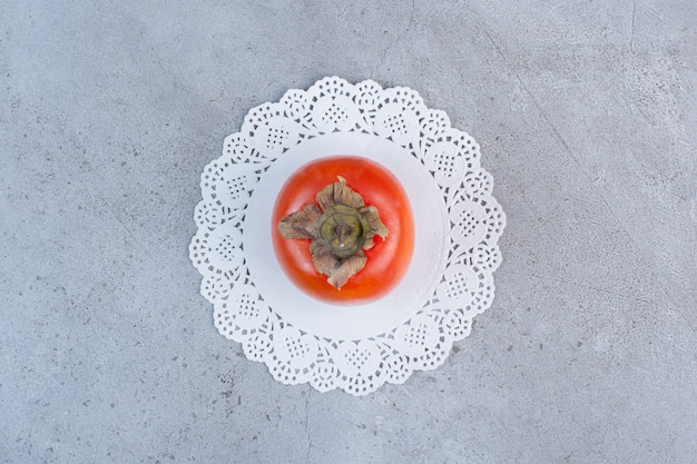 Juicy persimmon on a doily on marble background. 