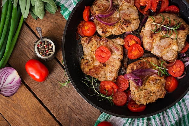 Бесплатное фото Сочный стейк из свинины с розмарином и помидорами на сковороде.