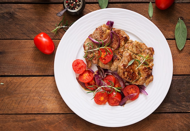 Juicy pork steak with rosemary and tomatoes on a white plate.