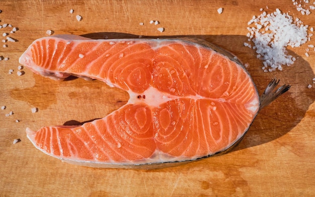 나무 커팅 보드에 있는 육즙이 많은 연어 스테이크는 핀란드식 생선 수프 아이디어 또는 생선 스테이크 레시피 배경 케토 다이어트 유기농 식품을 식탁에 자연 햇빛으로 올려줍니다.