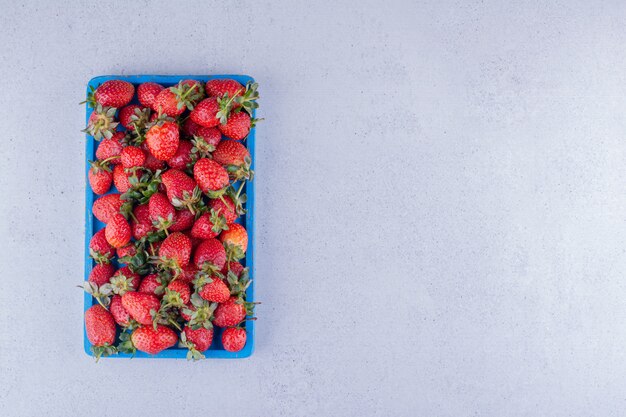 Juicy strawberries heaped into a blue tray on marble background. High quality photo
