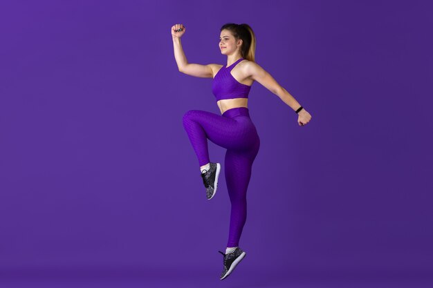 ジャンプ中。紫のモノクロのポートレートで練習する美しい若い女性アスリート。陽気な白人フィット モデル トレーニング。ボディビルディング、健康的なライフスタイル、美しさ、アクションのコンセプト。