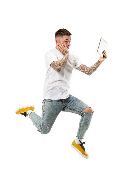 점프하는 동안 랩톱 컴퓨터를 사용하는 흰색 스튜디오 배경 위에 젊은 남자의 점프.