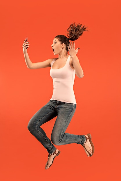 Free photo jump of young woman over blue studio background using laptop or tablet gadget while jumping. . gadget in modern life