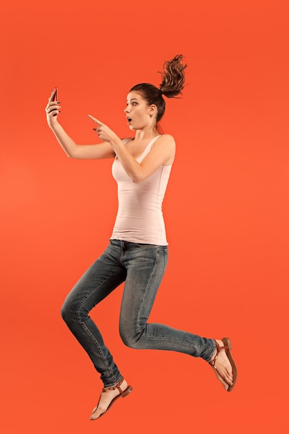 점프하는 동안 노트북 또는 태블릿 가제트를 사용하여 파란색 스튜디오 배경 위에 젊은 여자의 점프. 인간의 감정과 표정 개념.
