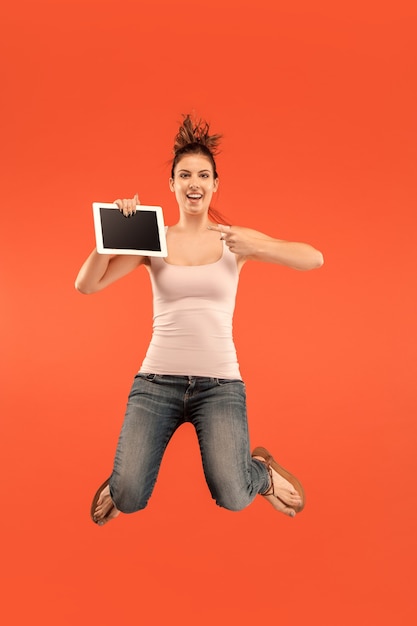Jump of young woman over blue studio background using laptop or tablet gadget while jumping. Runnin girl in motion or movement. 