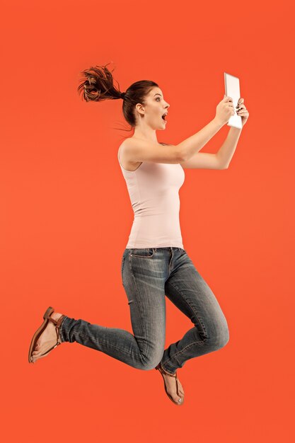 Jump of young woman over blue using laptop or tablet gadget while jumping. Runnin girl in motion or movement