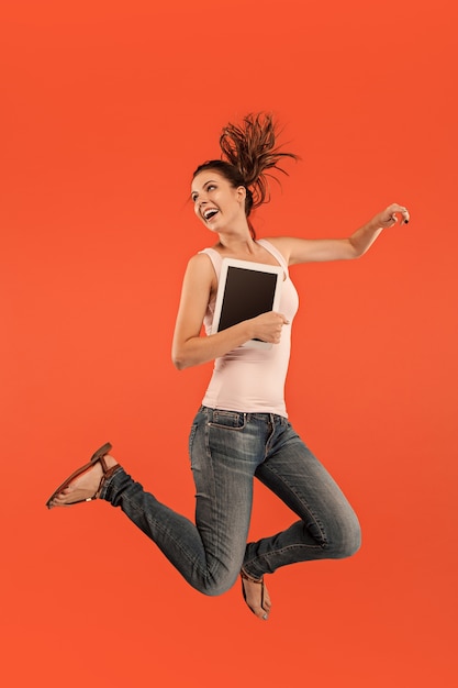 Прыжок молодой женщины над синим с помощью гаджета ноутбука или планшета во время прыжка. Девушка Runnin в движении или движении