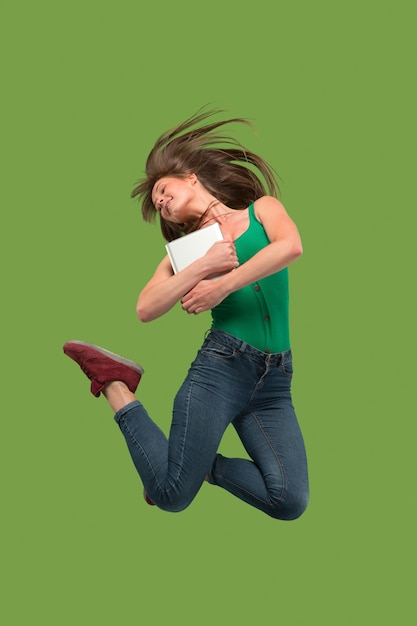 Free photo jump of young woman over green using laptop or tablet gadget while jumping. running girl in motion or movement