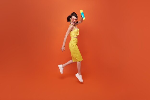 Jumping tourist woman traveling with water gun during Songkran festival studio background