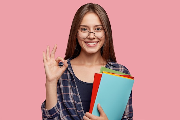 junge Geschäftsfrau, die gegen die rosa Wand mit Brille aufwirft