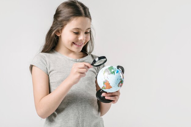 Junior girl studying globe with loupe