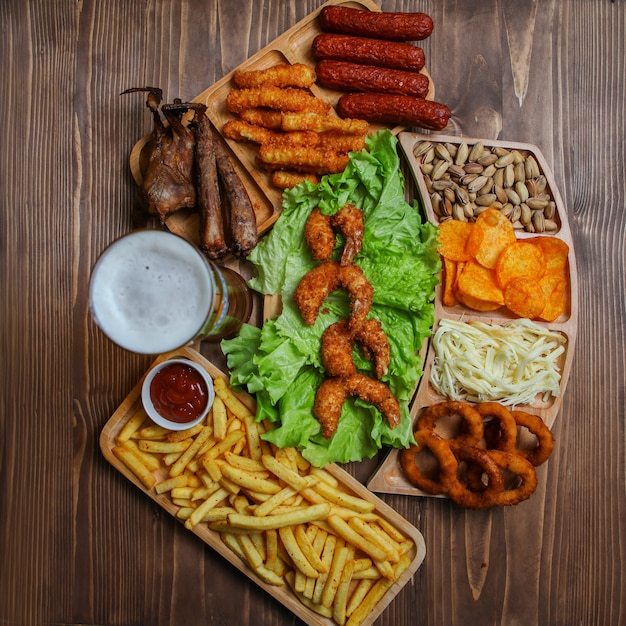 Junk food products in wooden plates with beer, cheese, barbecue, pistachio top view