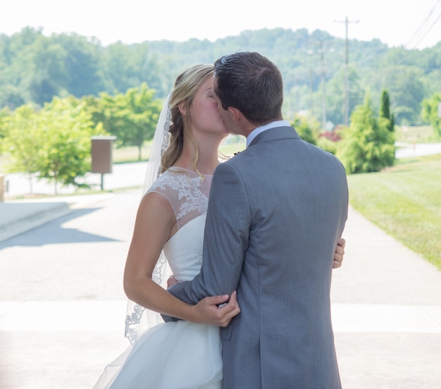 Just-married couple kissing in a garden surrounded by hills and greenery under the sunlight