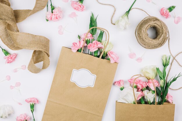ジュートリボン。トルコギキョウとカーネーションの花と白い背景の上のスレッドと紙の買い物袋のスプール