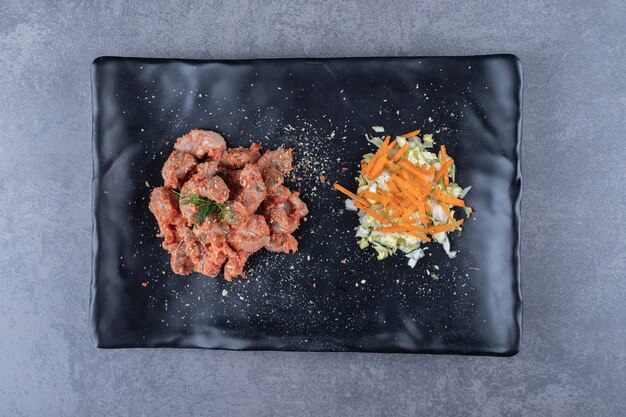 Kebab pieces and salad on black plate.