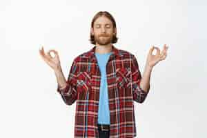 Free photo keep calm. calm and peaceful bearded blond man close eyes, meditating, holding hands sideways in om, zen nirvana gesture, practice yoga on white