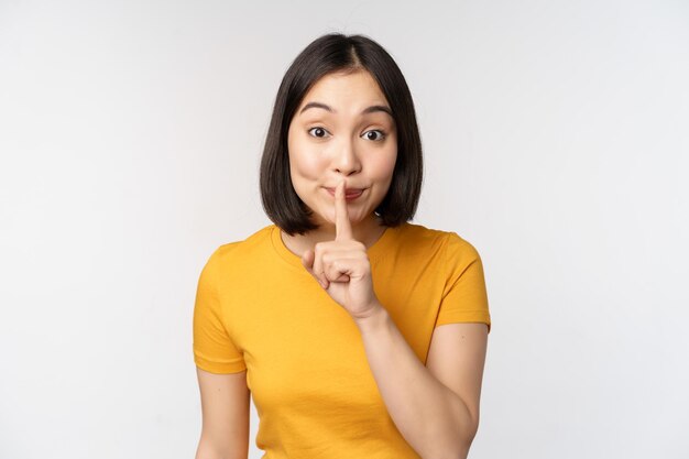 Keep quiet Cute asian woman make shhh gest showing shush hush sign press finger to lips silence standing over white background
