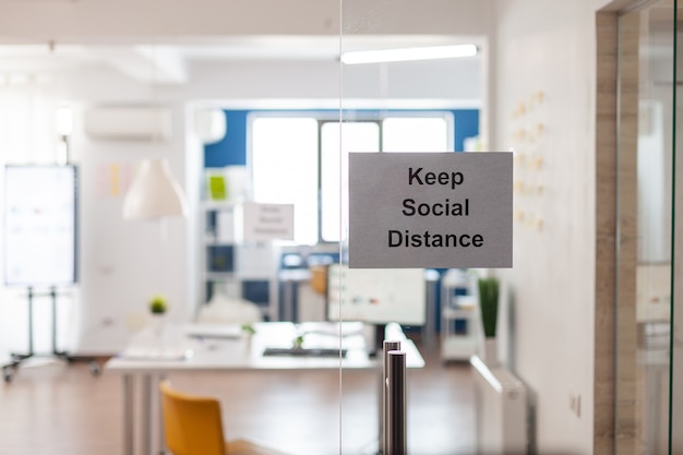 Keep Social Distance sign on glass wall in empty office during covid 19 coronavirus pandemic. Business workplace interior with nobody in it, economy crisis.