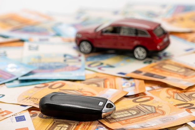 유로 지폐 더미에 열쇠와 빨간 장난감 자동차, 자동차 구매 또는 판매, 자동차 또는 보험 개념을 임대