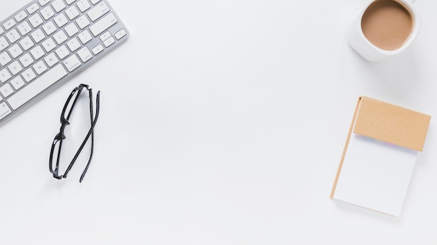 Keyboard and eyeglasses near notepad and coffee cup