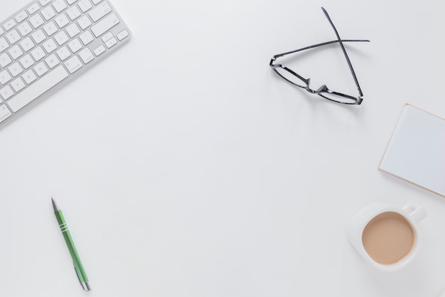 Keyboard and glasses near notes and coffee cup on desk