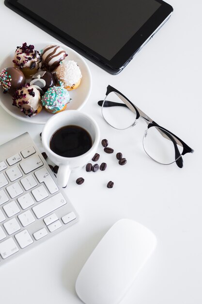 Keyboard near cup, tablet, eyeglasses, computer mouse and cookies on plate