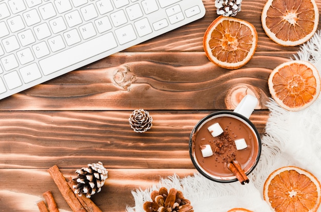 Keyboard near hot chocolate, oranges and bumps of tree