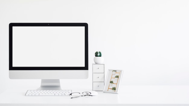 Keyboard near monitor, photo frame, cactus and eyeglasses on table