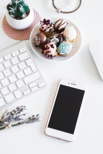 Keyboard near smartphone, bracelets, computer mouse and biscuits on plate