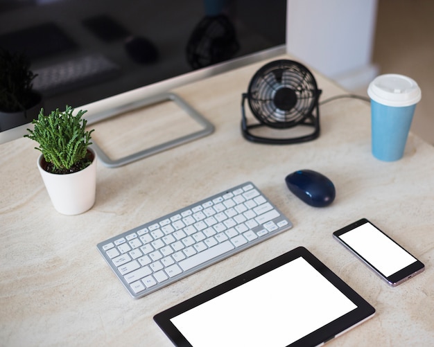 Keyboard near tablet, cup, smartphone, plant, monitor and cooling fan