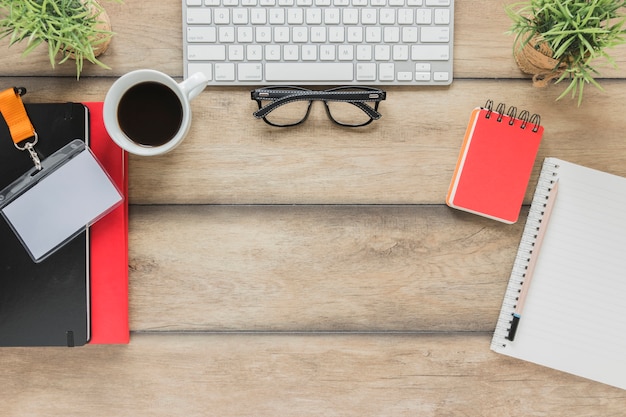 Keyboard with glasses near stationary and coffee cup on table