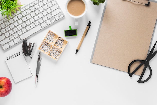 Keyboard with office supplies; tea and apple on white background