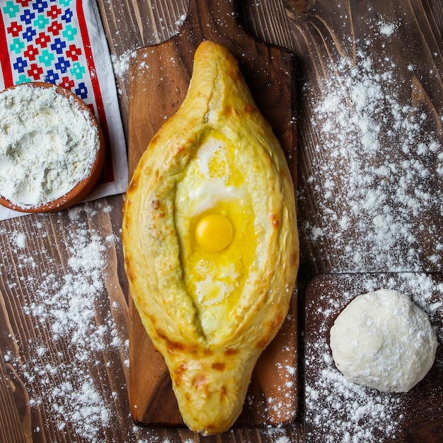 Khachapuri with kitchen towel, dough, flour on wooden and cutting board