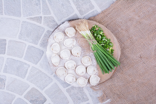 Foto gratuita ripieni khinkali nella farina serviti con un mazzetto di cipolla verde.