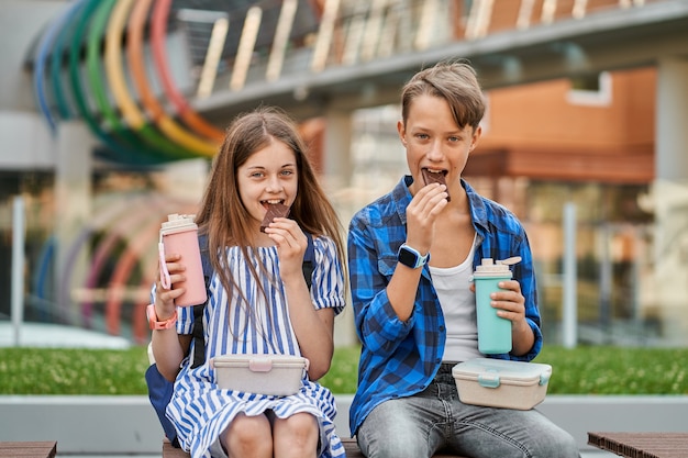 Free photo kid boy and kid girl eating chocolate and drink tea with lunchbox and thermos.