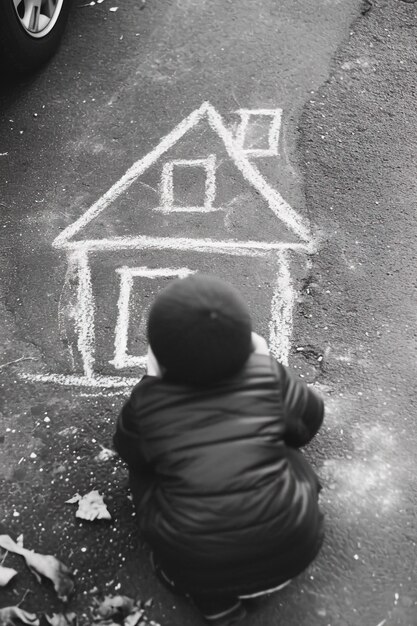 Ребёнок рисует дом с мелом на полу на открытом воздухе