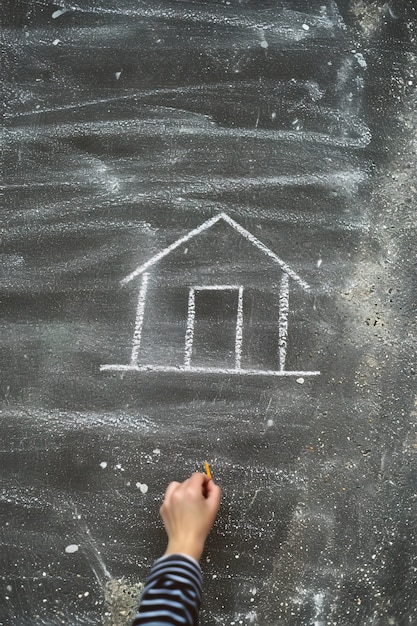 Kid drawing house with chalk on the road